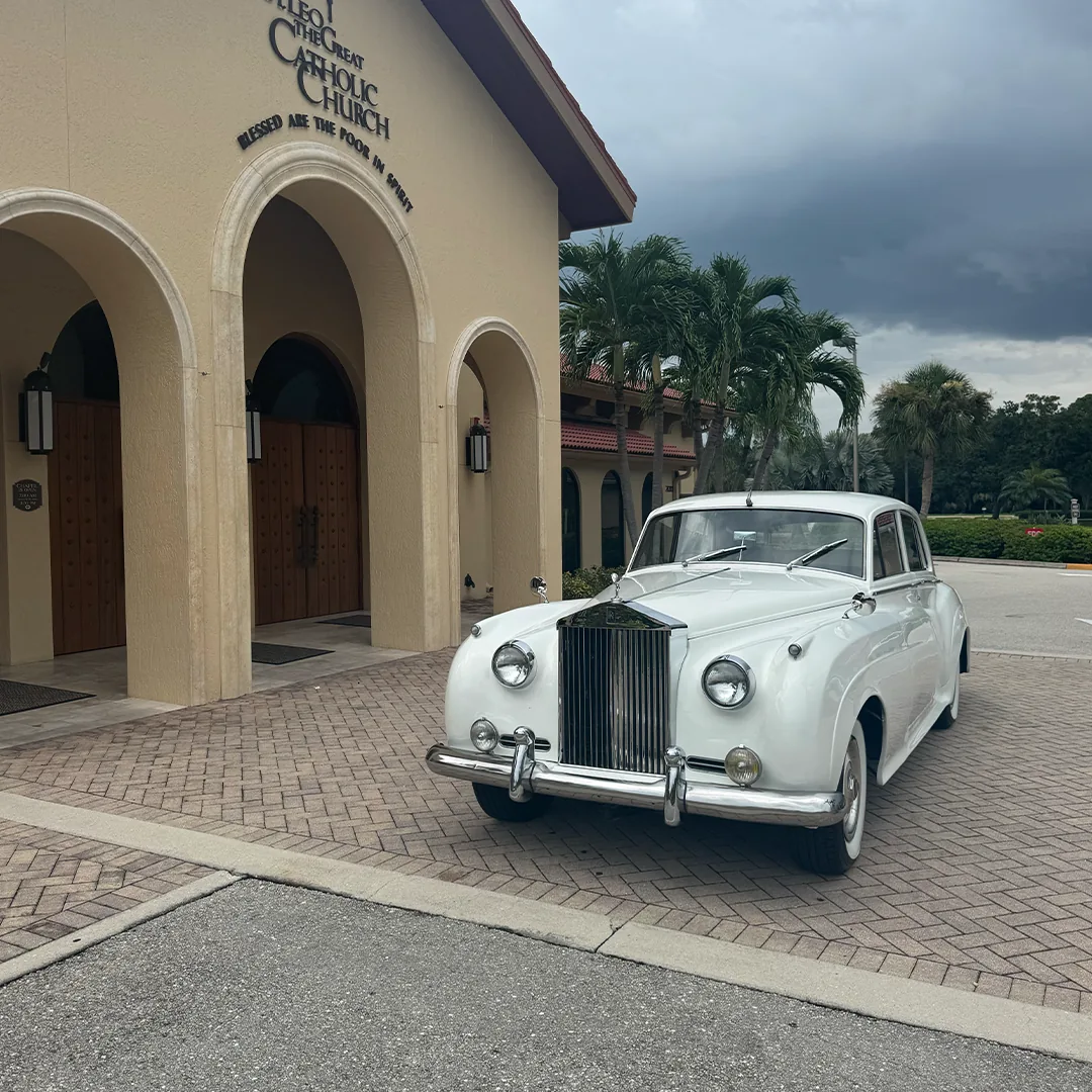 Front three quarter view of a vintage white Rolls Royce Silver Cloud II parked beneath the arches at St. Leo the Great Catholic Church in Bonita Springs, Florida