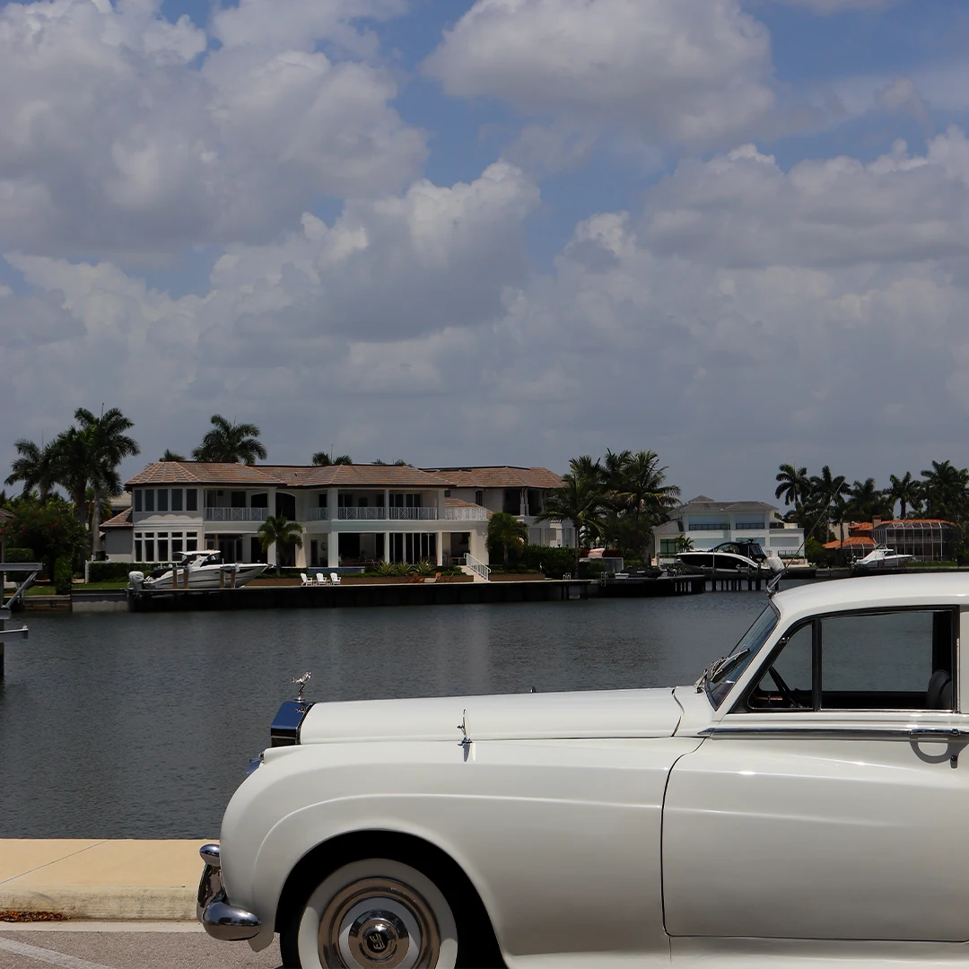 Side profile of a vintage white Rolls Royce Silver Cloud II along Naples Bay with waterfront estates in Florida