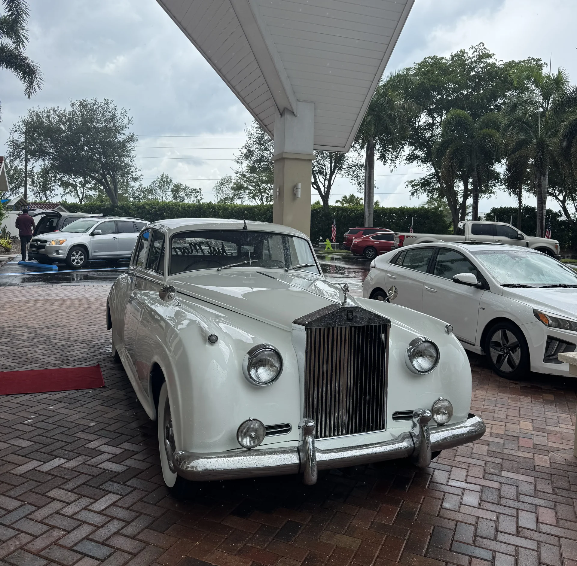 Just Married Rolls-Royce Silver Cloud II Gerleve Wedding Grace Lutheran Church Naples Florida September 2026 Cream white 1960 Rolls Royce Silver Cloud II with a Just Married windshield script parked under a porte-cochère for the Gerleve wedding at Grace Lutheran Church in Naples Florida