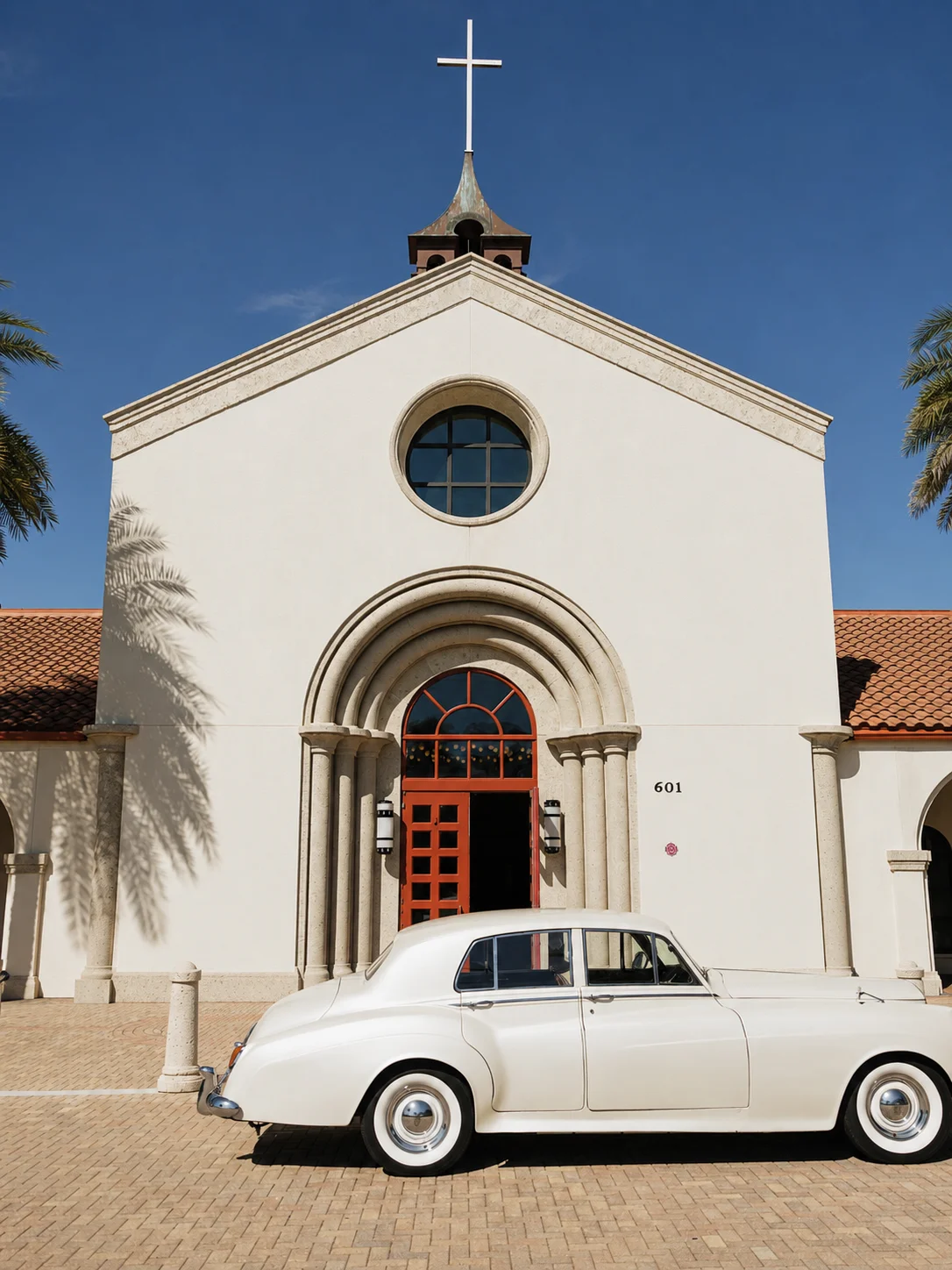 Saint William Catholic Church wedding venue — cream-white 1960 Rolls-Royce Silver Cloud II in front of the arched red doors and bell tower in Naples, Florida