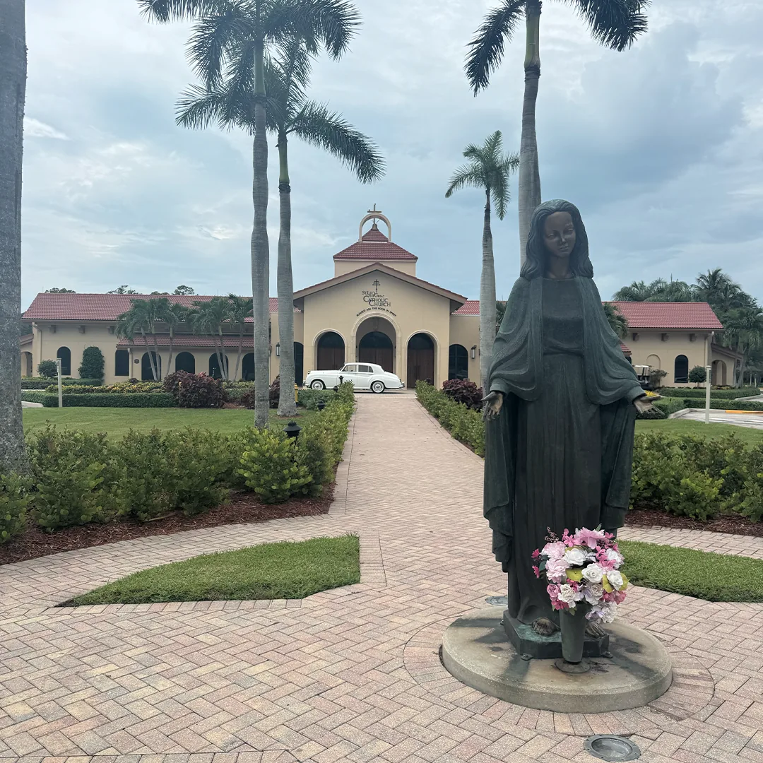 Statue of Mary in the foreground with a vintage white Rolls Royce Silver Cloud II parked at St. Leo the Great Catholic Church in Bonita Springs, Florida