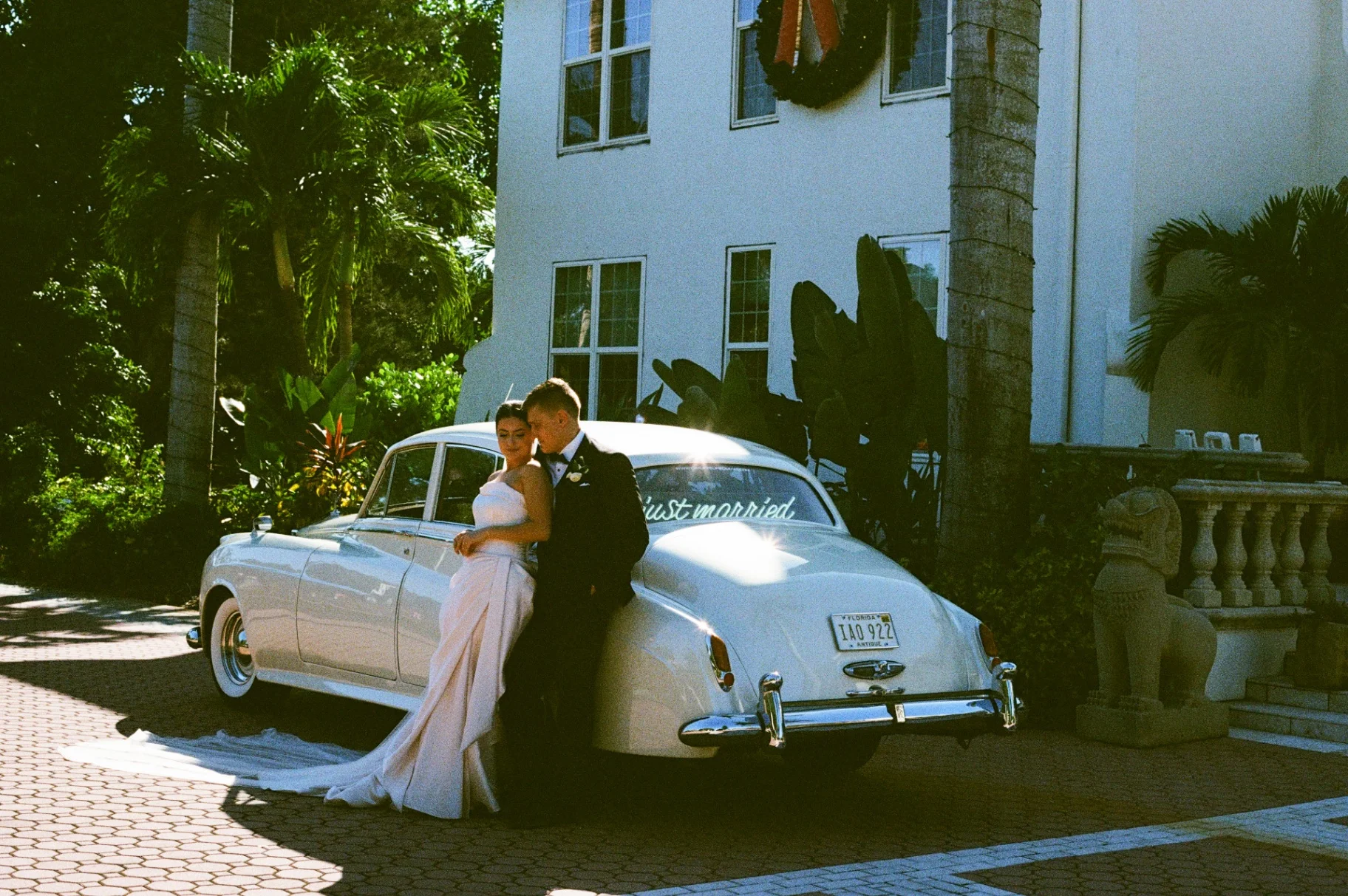 Shangri-La Springs wedding — newlyweds leaning against the rear of the cream-white 1960 Rolls-Royce Silver Cloud II with 'just married' script at the Bonita Springs venue