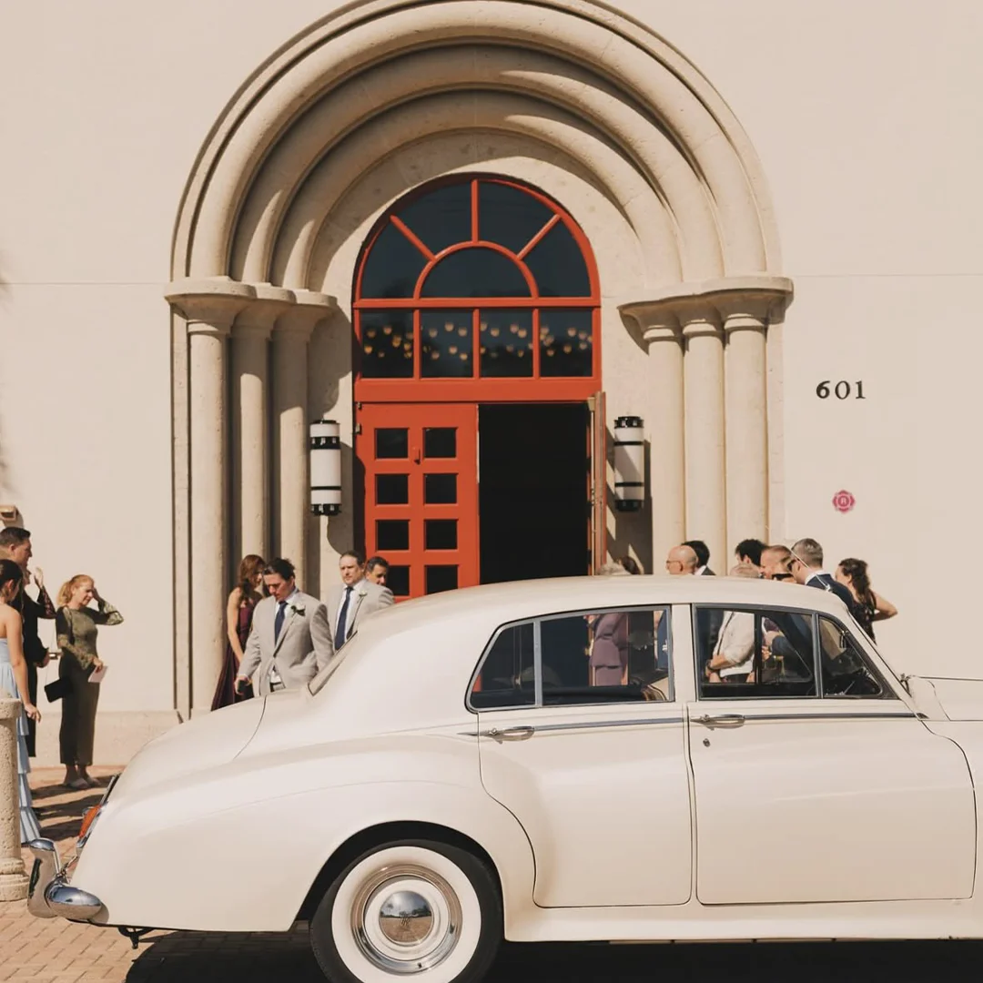 Vintage cream white Rolls Royce Silver Cloud II at Saint William Catholic Church wedding venue with red doors in Naples, Florida