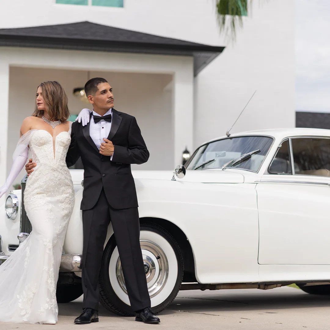 Bride in a lace gown and groom in a tuxedo leaning against the vintage cream white Rolls Royce Silver Cloud II at a 1920s era styled shoot at Rock Manor