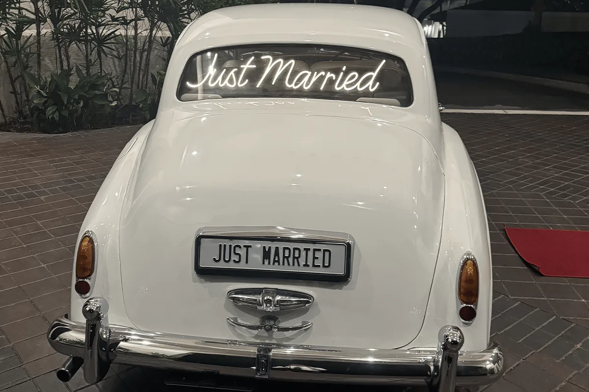 Just Married Neon Sign Rolls-Royce Silver Cloud II Night Wedding Exit Bonita Springs FL Rear view of a cream white vintage Rolls-Royce Silver Cloud II with a glowing Just Married neon sign in the rear window and a Just Married plate at night in Bonita Springs Florida
