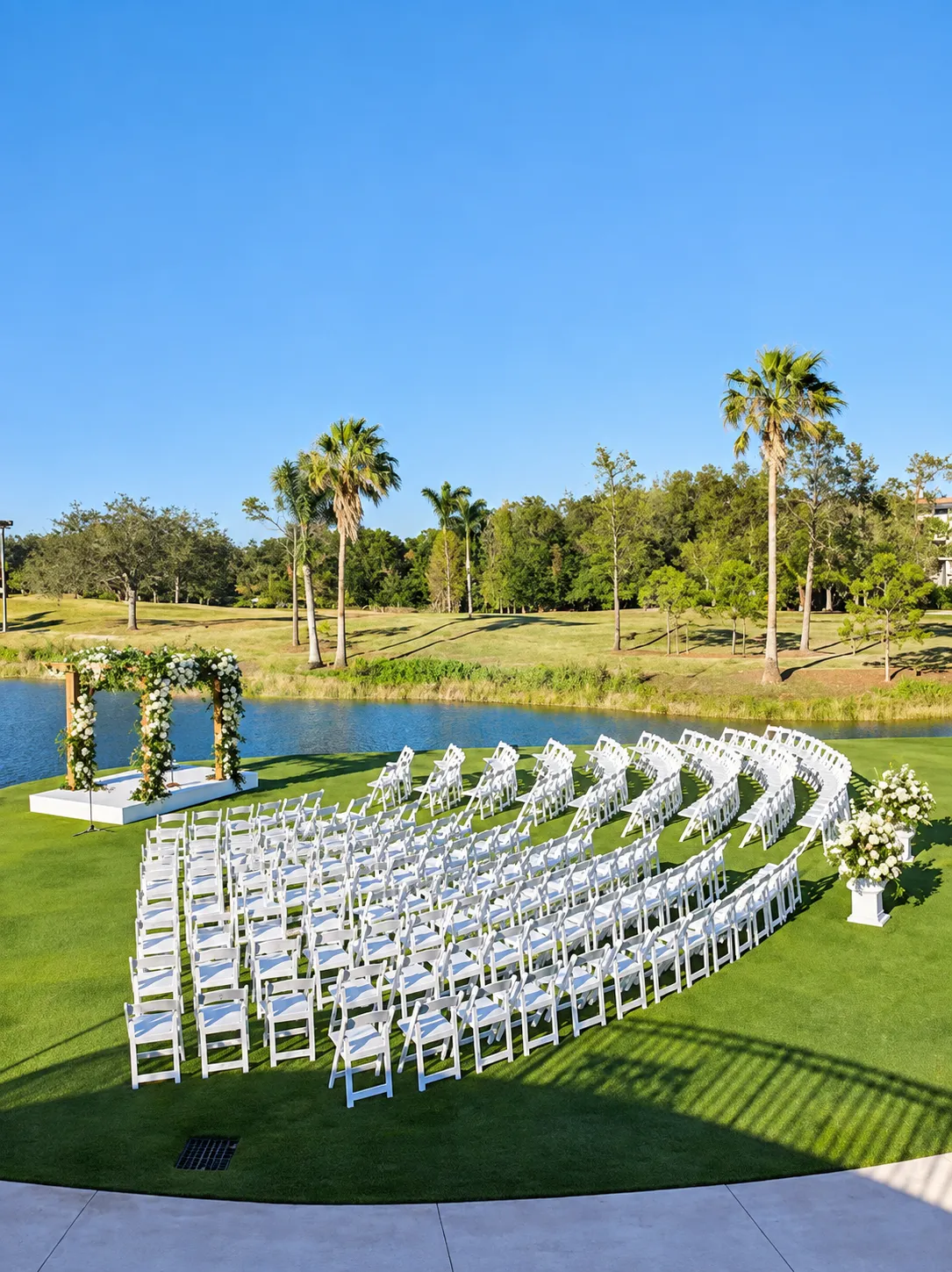 Grey Oaks Country Club wedding venue in Naples, Florida — outdoor ceremony with white floral arch and chairs on a manicured lawn overlooking a golf-course lagoon