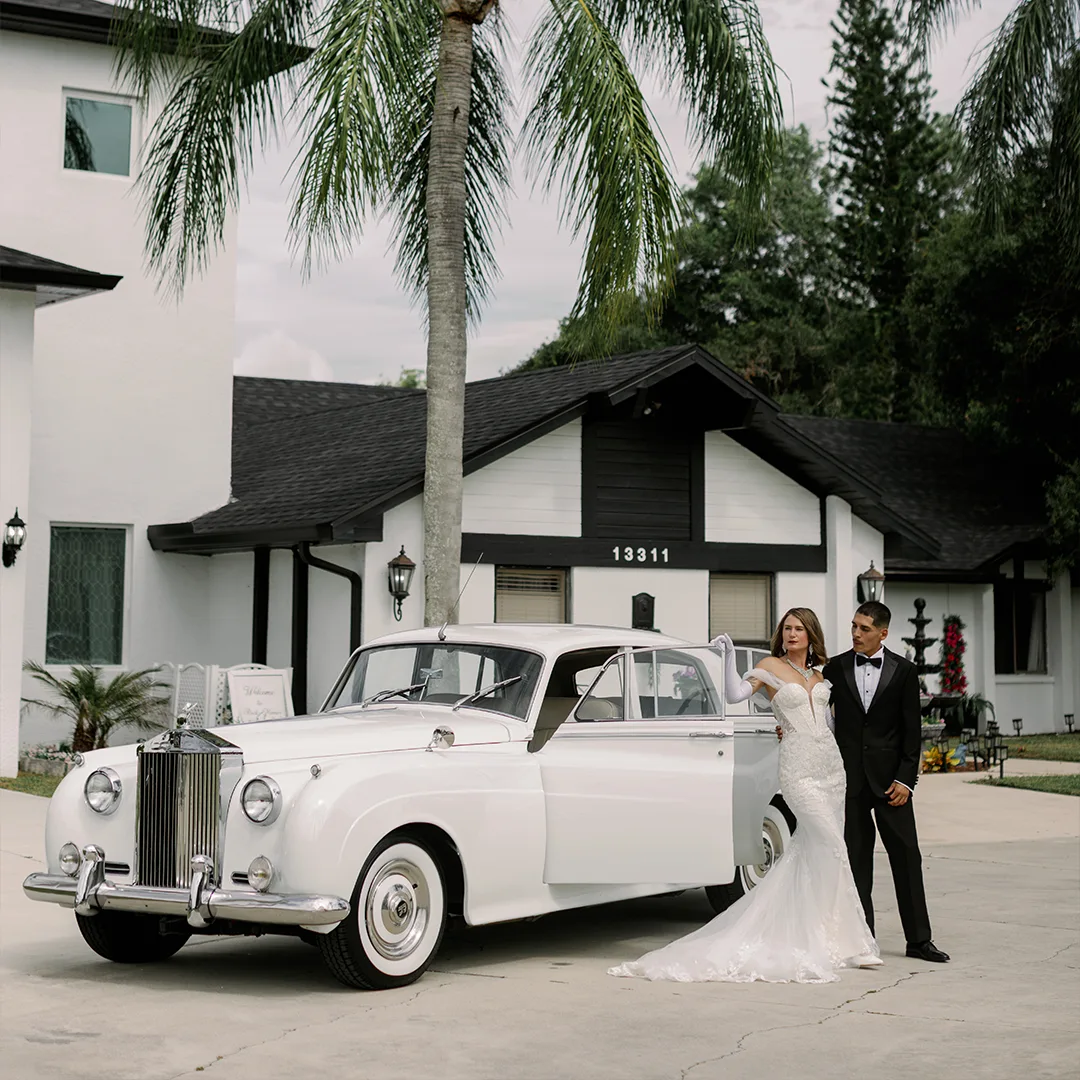 Bride and groom standing beside a vintage cream white Rolls Royce Silver Cloud II on the driveway at Rock Manor wedding venue in Fort Myers, Florida