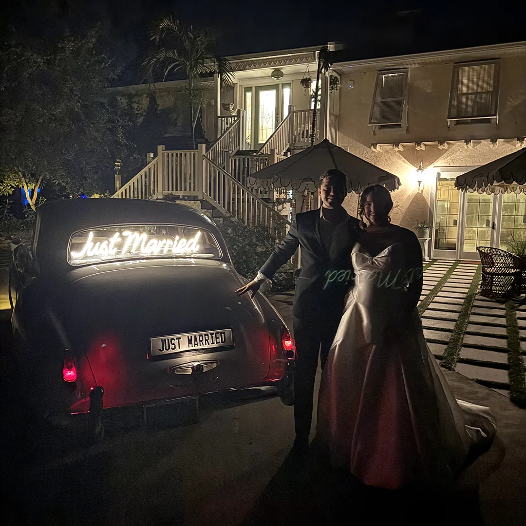 Just Married Rolls Royce Silver Cloud II Night Getaway Naples Florida Wedding Gift Surprise Bride and groom beside the rear of a vintage cream white Rolls Royce Silver Cloud II with a glowing Just Married neon sign on their wedding night in Naples Florida