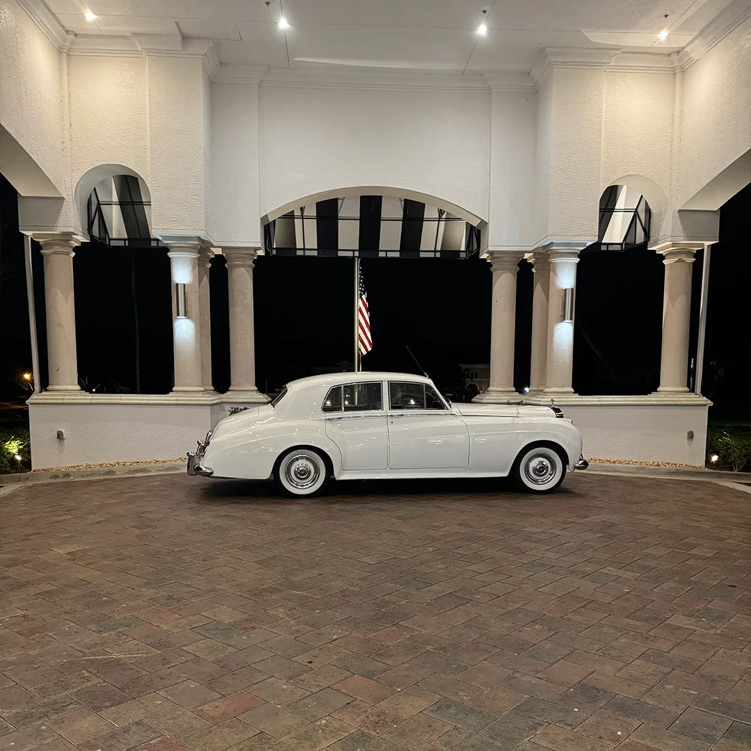 Vintage white 1960 Rolls-Royce Silver Cloud II parked beneath the illuminated arched portico at The Strand in Naples Florida for the Rieth wedding getaway