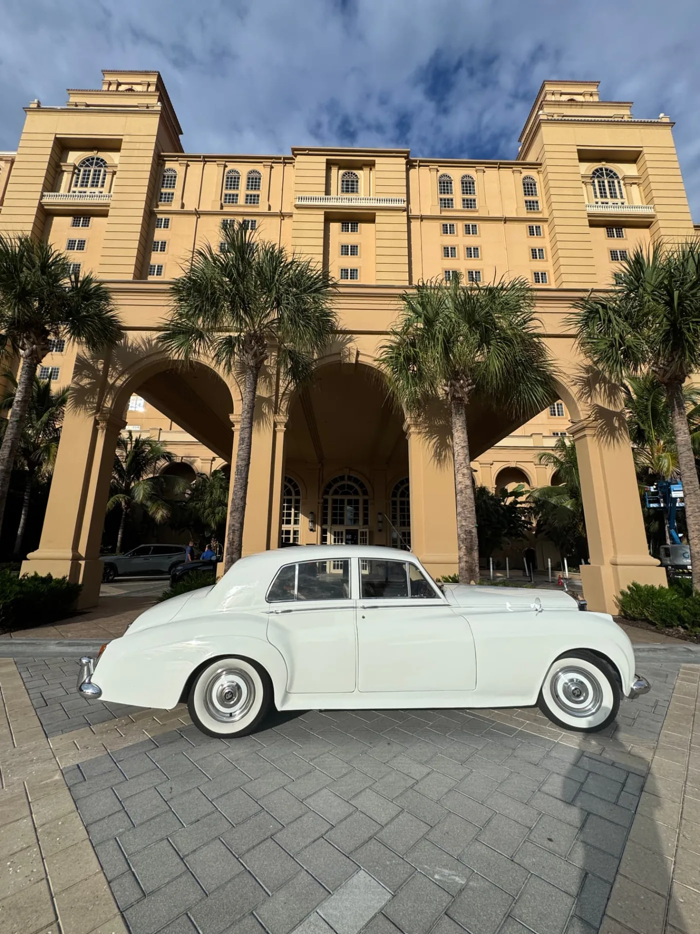 The Ritz-Carlton, Naples Wedding — Naples, FL Cream-white 1960 Rolls-Royce Silver Cloud II parked in full side profile beneath the arched porte-cochère of The Ritz-Carlton, Naples wedding venue on Vanderbilt Beach in Naples Florida