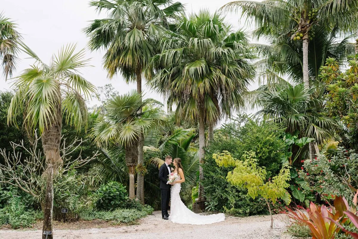 Bride and groom in wedding attire on a garden path surrounded by lush palms and tropical foliage at Naples Botanical Garden in Naples, Florida