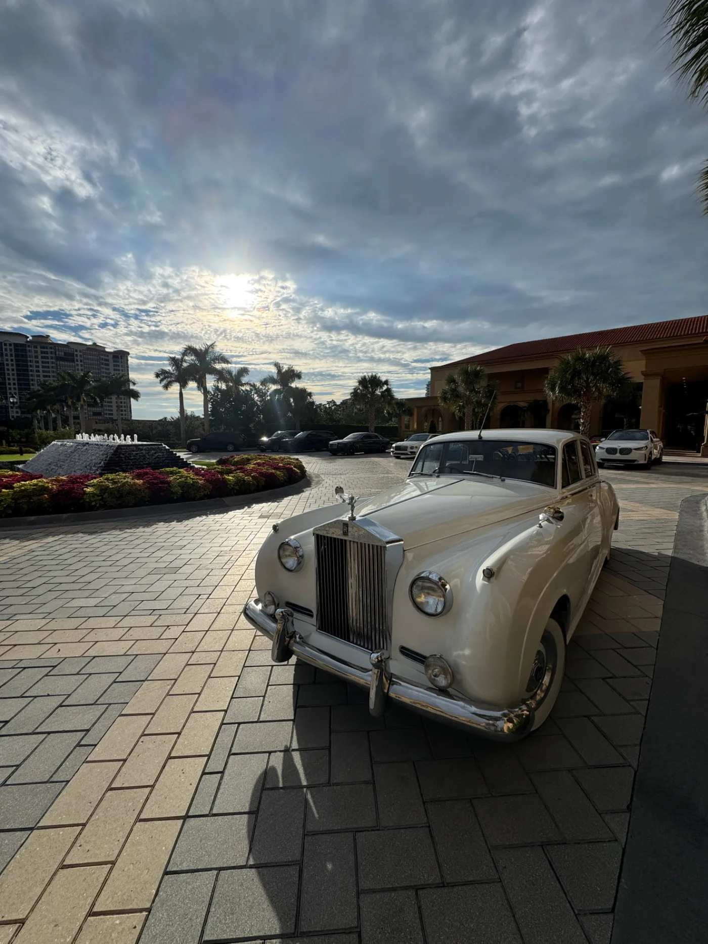 The Ritz-Carlton, Naples Wedding — Naples, FL Cream-white 1960 Rolls-Royce Silver Cloud II waiting on the brick courtyard driveway beside the tiered fountain at The Ritz-Carlton, Naples wedding venue in Naples Florida