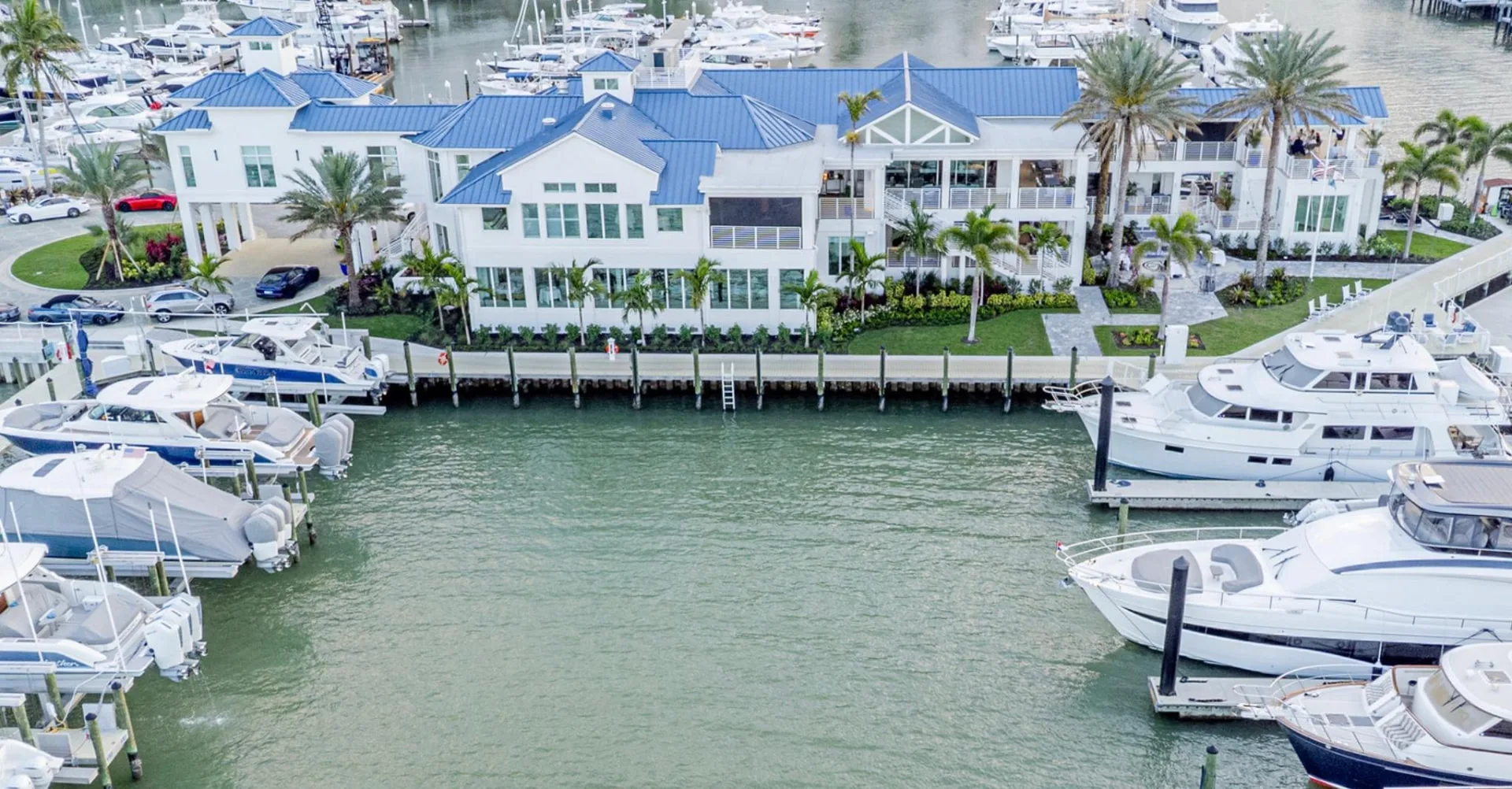 Marco Island Yacht Club wedding venue — aerial view of the white clubhouse with blue roofs and yachts docked along the marina on Marco Island, Florida