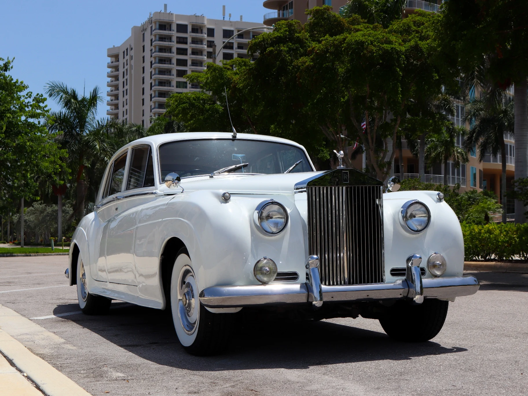 Front view of vintage white 1960 Rolls-Royce Silver Cloud II wedding transportation in Naples Florida with palm trees and coastal high-rise backdrop