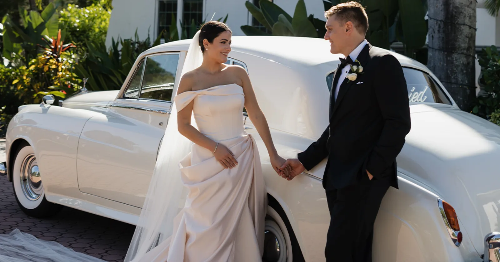 Bride and Groom Rolls-Royce Portrait Shangri-La Springs Bonita FL Bride and groom holding hands beside a vintage cream white 1960 Rolls-Royce Silver Cloud II at Shangri-La Springs wedding venue in Bonita Springs Florida