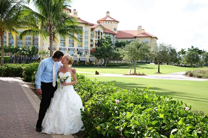Bride and groom leaning in to kiss with a bouquet of white lilies on the lawn outside the Tiburon Golf Club clubhouse in Naples Florida
