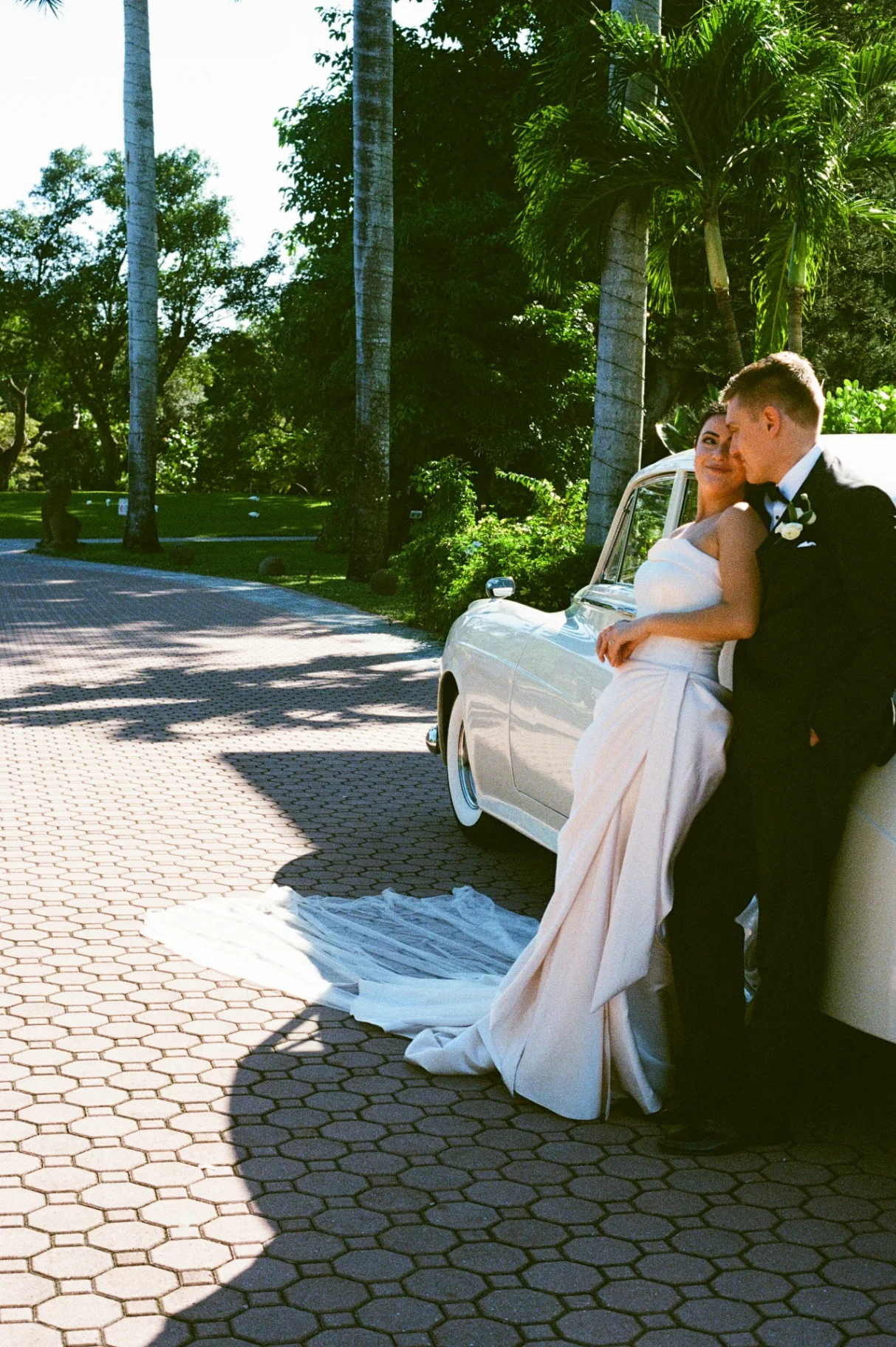 Shangri-La Springs wedding — bride and groom embracing beside the cream-white 1960 Rolls-Royce Silver Cloud II on the brick-paved drive of the Bonita Springs venue
