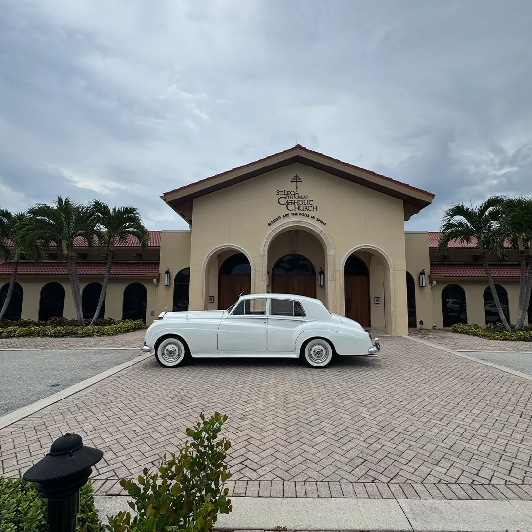 Full side profile of a vintage white Rolls Royce Silver Cloud II parked in front of St. Leo the Great Catholic Church in Bonita Springs, Florida