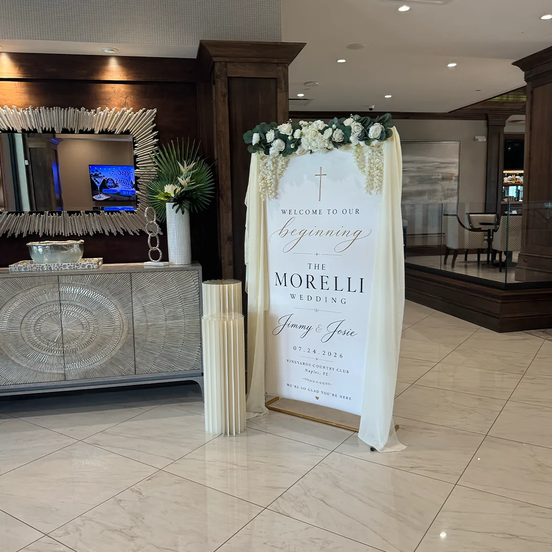Elegant welcome sign for Jimmy and Josie Morelli's wedding at Vineyards Country Club in Naples Florida draped in ivory florals and greenery