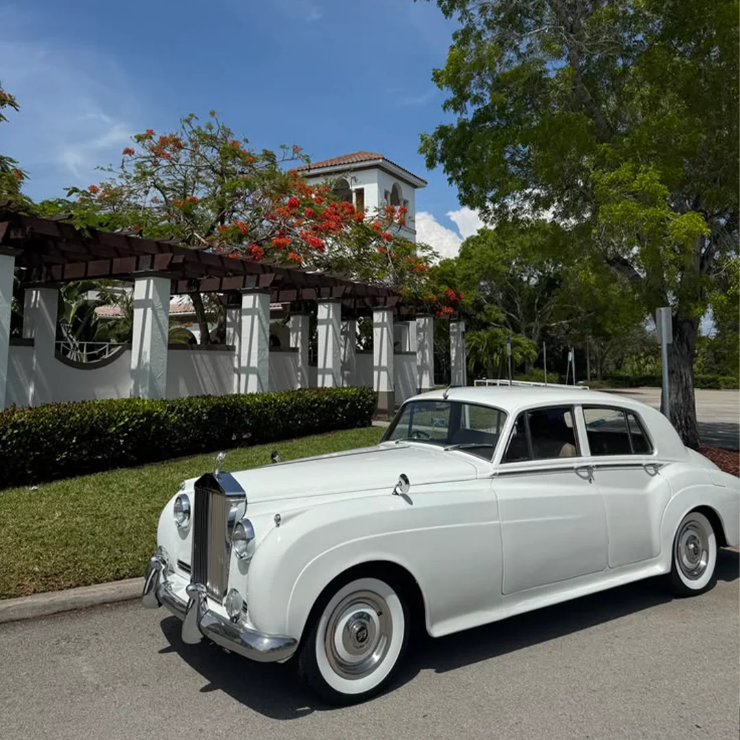 Vintage white Rolls Royce Silver Cloud II parked beneath a Mediterranean tower and flowering trees in Naples, Florida