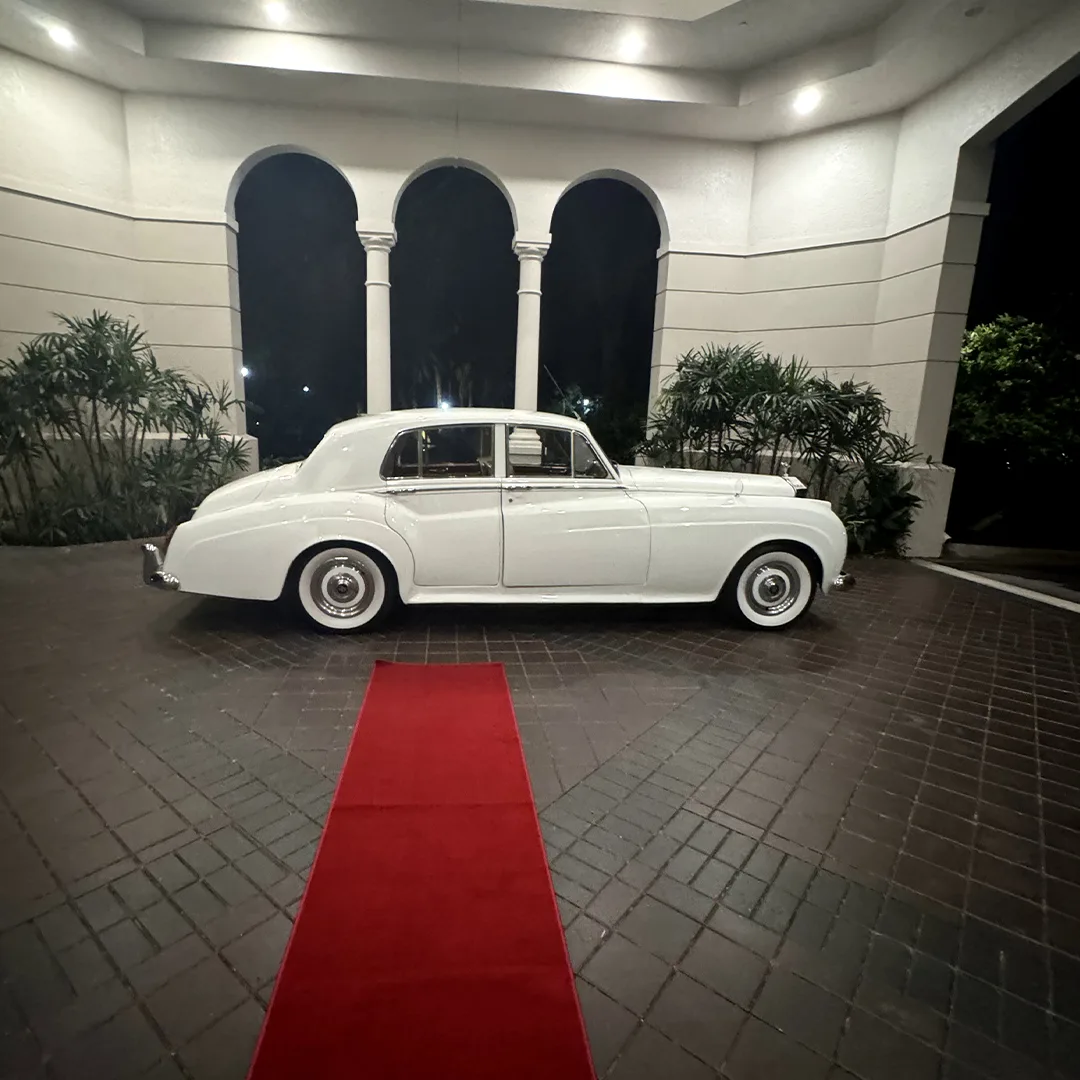 Vintage white Rolls Royce Silver Cloud II side profile beside a red carpet beneath illuminated arches at night at Palmira Golf Club in Bonita Springs, Florida