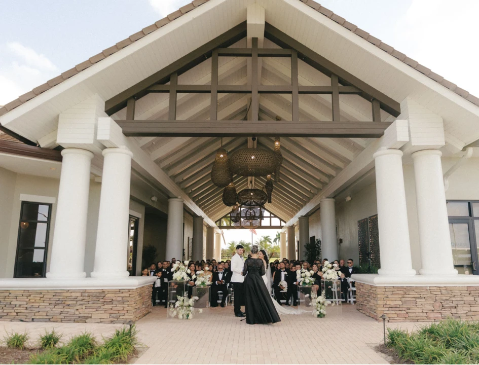 The Quarry Beach Club wedding venue — grand covered pavilion with tall white columns, wooden beams, and elegant chandeliers during an outdoor ceremony in Naples, Florida