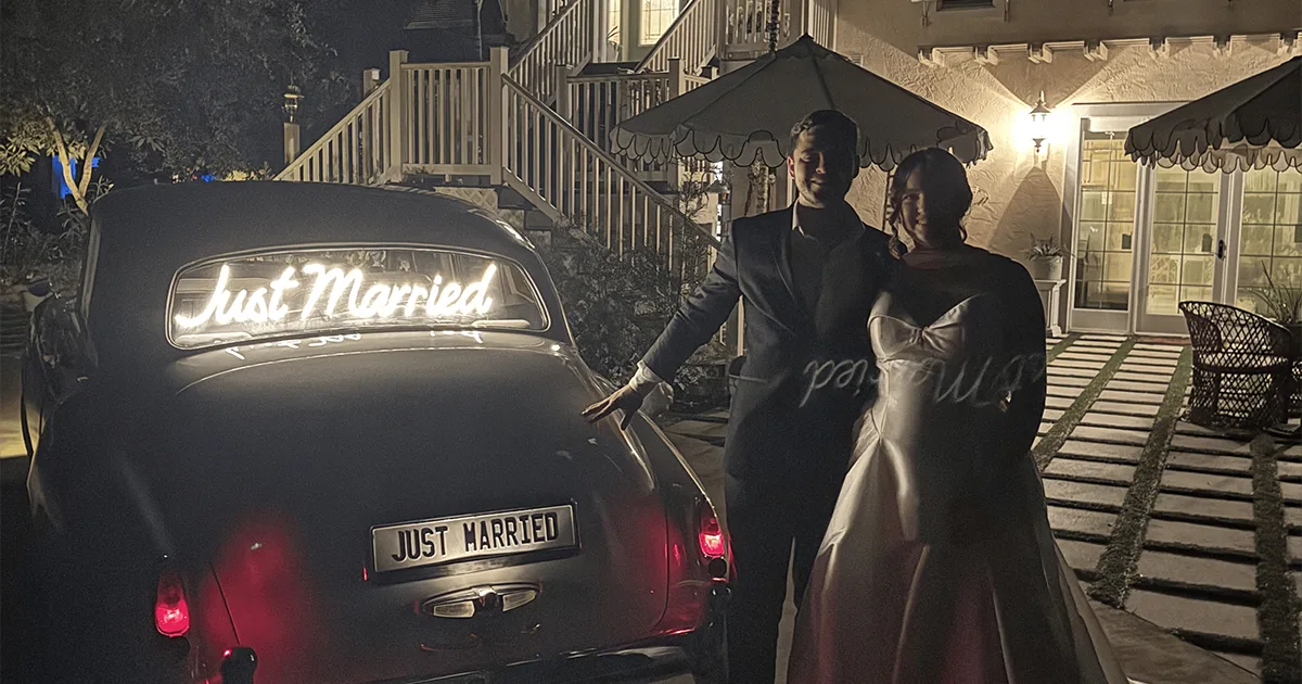 Newlyweds standing beside a vintage Rolls-Royce Silver Cloud II with a glowing Just Married neon sign at night in Naples Florida