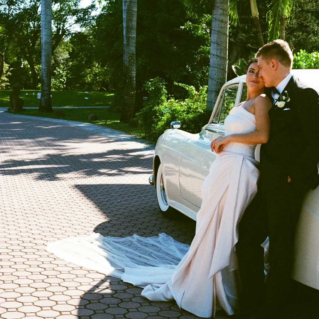 Bride with long veil resting on a vintage cream white Rolls Royce Silver Cloud II with groom at Shangri-La Springs in Bonita Springs, Florida