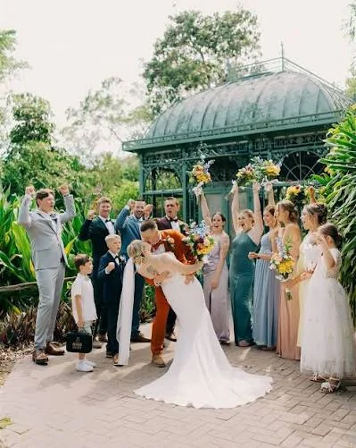 Bride and groom sharing a kiss as their wedding party cheers on a brick courtyard in front of the ornate green glasshouse at Wonder Gardens in Bonita Springs, Florida