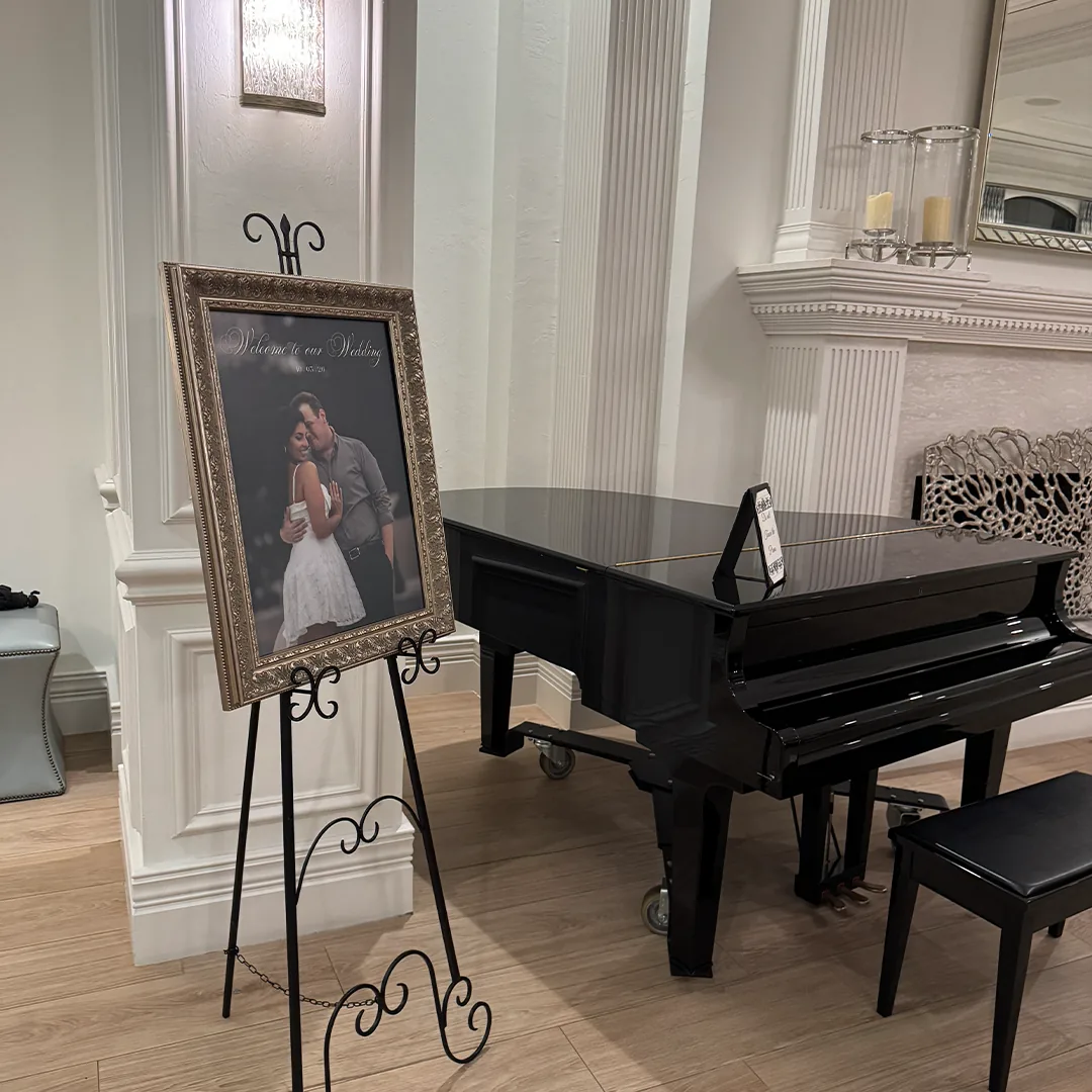 The Club at Grandézza Wedding — Estero, FL The Club at Grandézza wedding reception — gold-framed welcome sign on an easel beside a black grand piano in the Estero, Florida clubhouse