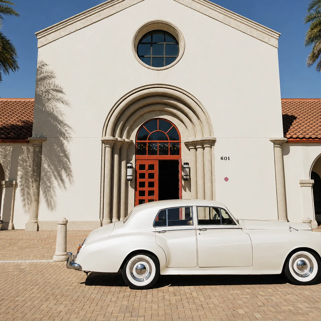 Side profile of a vintage cream white Rolls Royce Silver Cloud II parked in front of Saint William Catholic Church with red arched doors in Naples, Florida