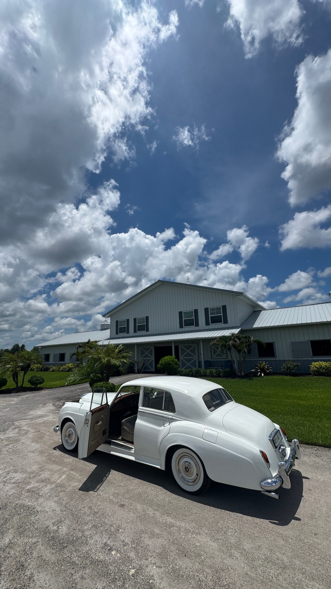 Shore Acres Farm Wedding — Naples, FL Vintage white Rolls-Royce Silver Cloud II with door open in front of the white equestrian barn at Shore Acres Farm in Naples, Florida