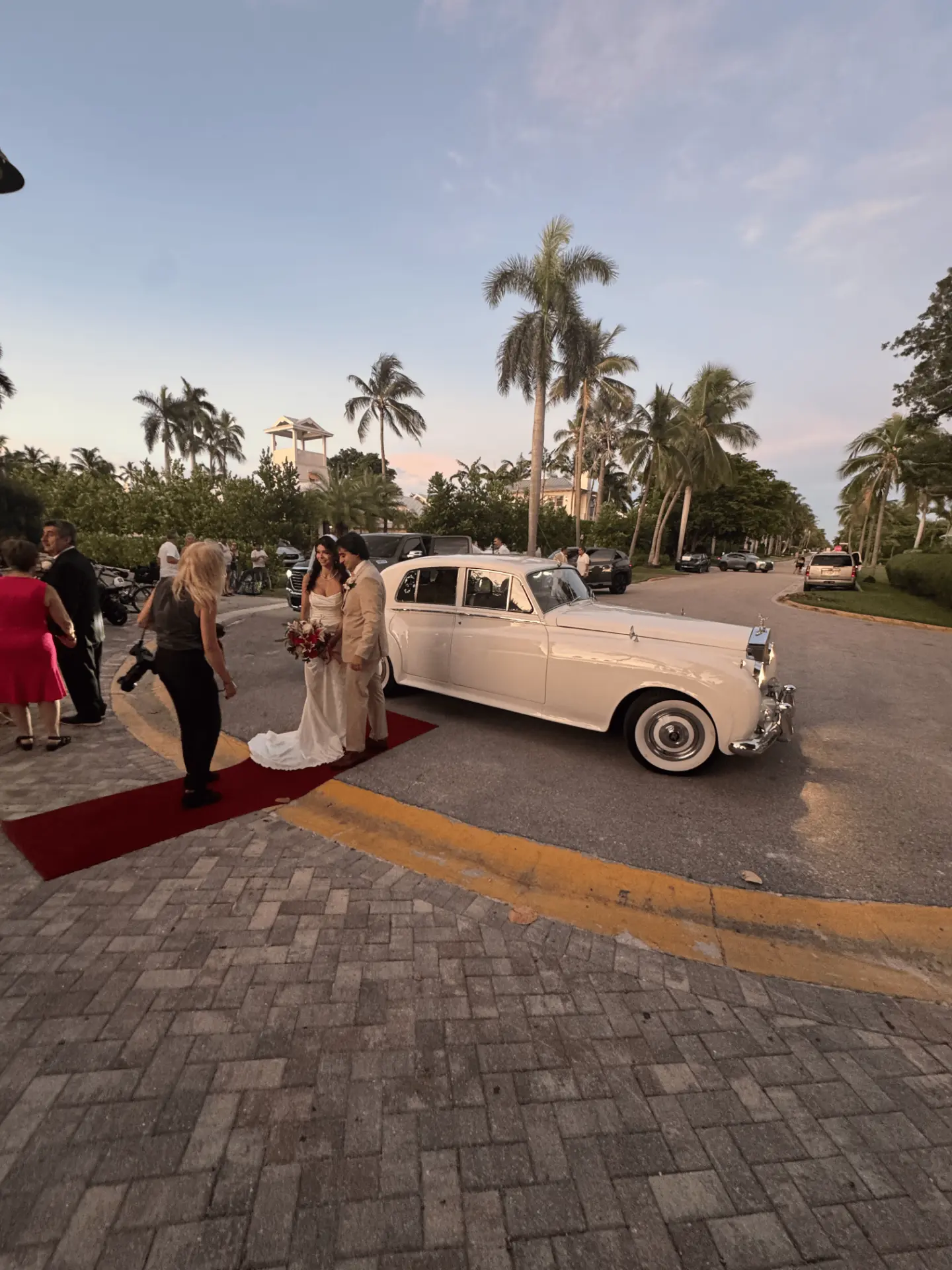 Bride and groom standing beside a cream white vintage Rolls-Royce Silver Cloud II on a red carpet at their beach wedding on 8th Ave South in Naples Florida