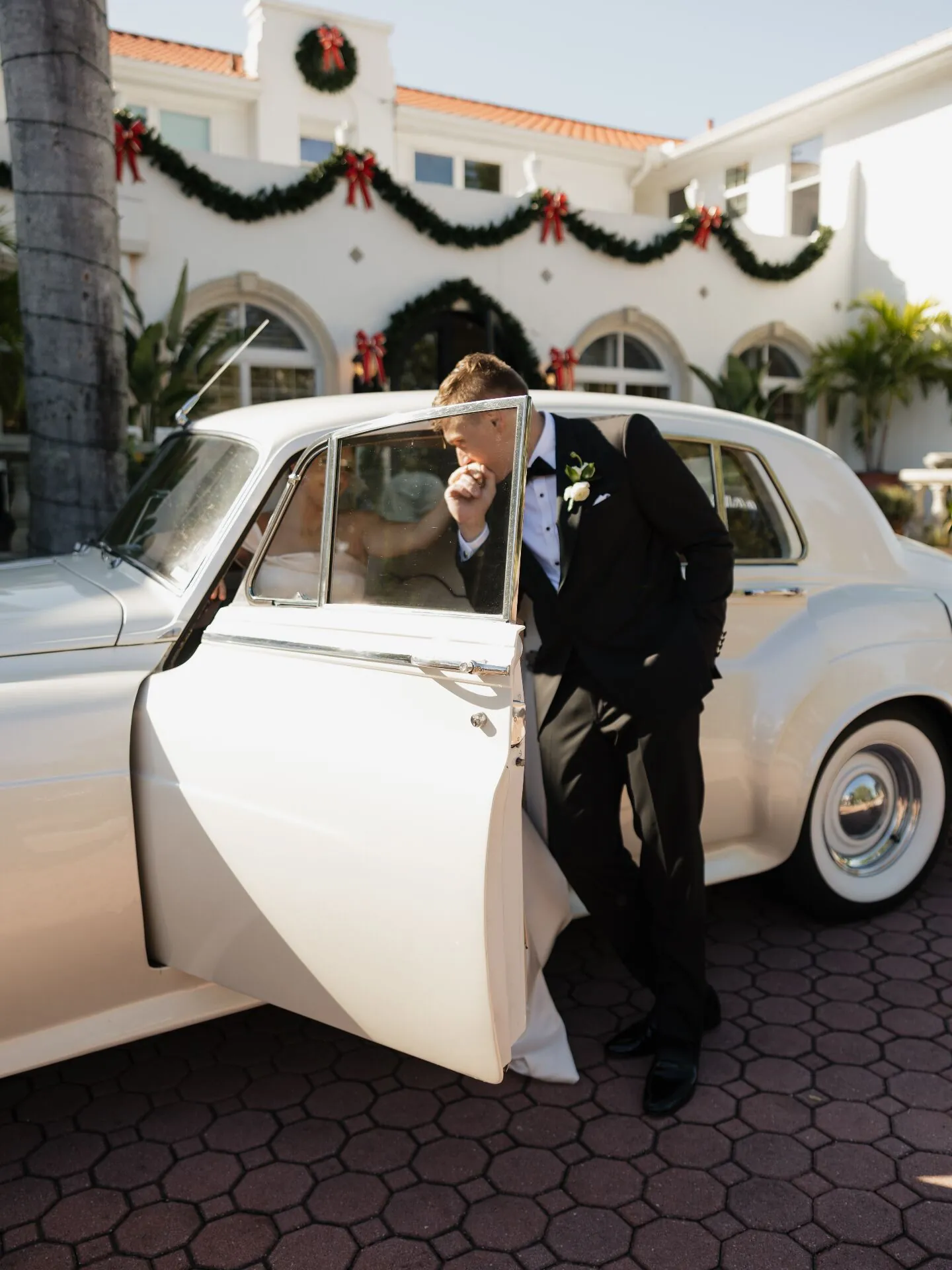 Groom kissing bride's hand beside vintage Rolls-Royce wedding rental in Fort Myers Florida