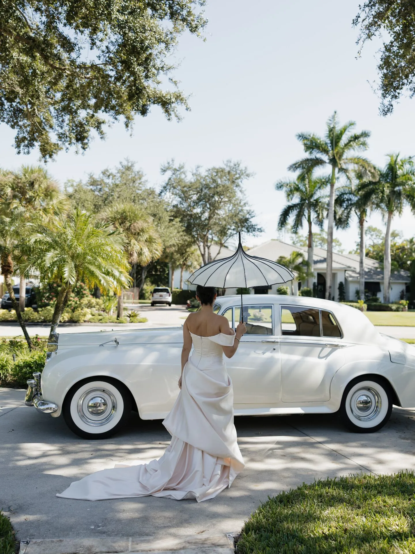 Bride with parasol beside vintage Rolls-Royce wedding rental under Fort Myers palm trees